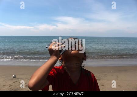 Un enfant utilise des morceaux de verre noir pour observer une éclipse solaire partielle sur la côte de la ville de Lhokseumawe.le phénomène d'éclipse solaire est partiellement vu dans la ville de Lhokseumawe, province d'Aceh. Le phénomène de l'éclipse solaire d'anneau (GMC) est en partie différent cette année de l'année précédente parce qu'il coïncide avec le solstice d'été, appelé l'anneau de feu de Solstice. Selon l'Institut de l'aviation et de l'espace (Lapan), le Solstice Ring of Fire est assez rare parce qu'il s'est produit pour la dernière fois en 1648 et sera répété le 21 juin 2039. Banque D'Images