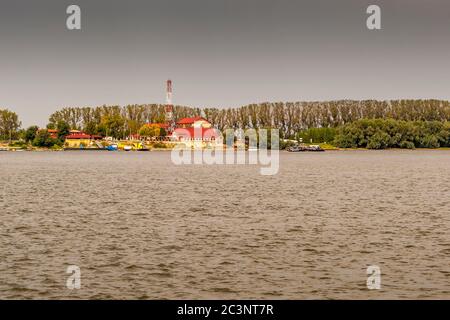 Des bâtiments aux toits rouges et un mât de radio marquent la ville de Silistra, sur la rive bulgare du Danube, avec de petits bateaux amarrés devant elle. Le Danube forme la frontière entre la Roumanie et la Bulgarie sur une longueur d’environ 470 kilomètres. Les seuls ponts permanents se trouvent à Giurgiu/Ruse et à Vidin/Calafat ; ailleurs, des ferries locaux pour voitures assurent la traversée, ici entre la rive roumaine près de Călărași et Silistra, en Bulgarie. Banque D'Images