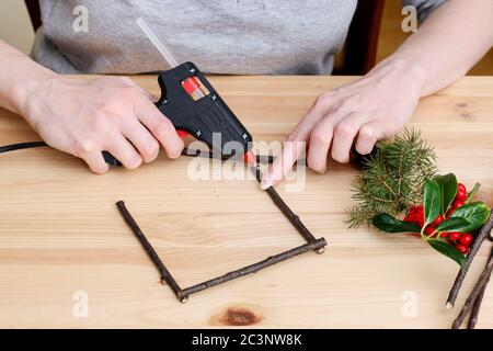 Fleuriste au travail: Femme montre comment faire miniature cadre de fenêtre en bois décoré de houx (ilex), de sapin et de cônes. Décoration de Noël traditionnelle. S Banque D'Images