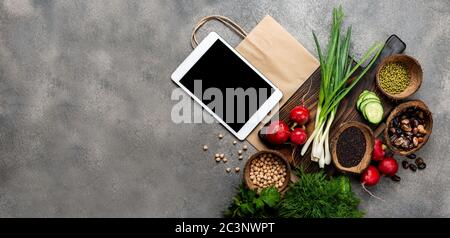 Commande, livraison de nourriture. Légumes produits alimentaires biologiques sur un panneau en bois avec un ordinateur tablette et un sac de papier avec espace de copie sur le gris Banque D'Images