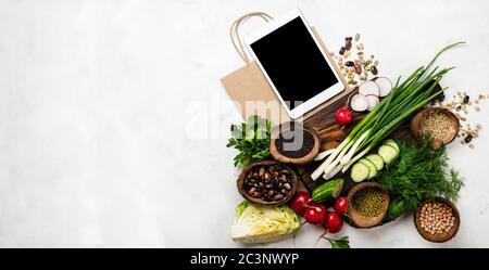 Commande, livraison de nourriture. Produits alimentaires biologiques sur un panneau en bois avec un ordinateur tablette et un sac de papier sur fond blanc avec espace de copie. Bannière Banque D'Images