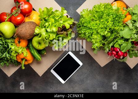 Commander et livrer des aliments. Produits biologiques en boîtes et ordinateur tablette sur la table sur fond gris. Vue de dessus Banque D'Images