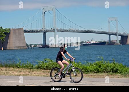 À l'ombre du pont Throgs Neck, une femme asiatique américaine portant un masque chirurgical tout en faisant du vélo sur un sentier dans Little Bay Park, Whitestone Queens Banque D'Images