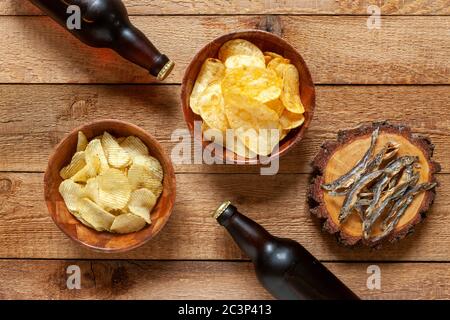 Deux bouteilles de bière avec des chips et du poisson-perlan séché sur fond de bois de pierre sombre Banque D'Images