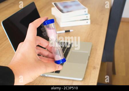 main saisissant un sablier dans le bureau. Ordinateur portable et livre sur la table Banque D'Images