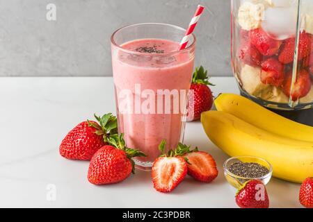 Smoothie fraise et banane ou milkshake dans un verre avec une paille et un mélangeur avec des fruits frais pour faire une boisson saine. Concept de cuisine Banque D'Images