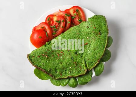 Omelette aux épinards verts avec tomates, épices et herbes sur fond de marbre blanc. Nourriture pour keto. Vue du dessus Banque D'Images