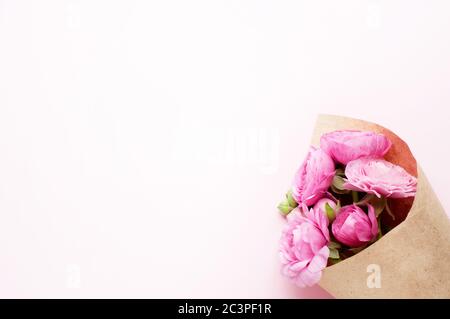 Un bouquet de fleurs de ranunculus roses en papier d'emballage artisanal sur fond rose. Vue de dessus, espace de copie. Concept Fête des mères, Fête de la famille, Saint-Valentin Banque D'Images