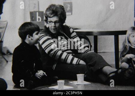 Belle photo vintage des années 70 en noir et blanc d'un garçon assis sur le sol en s'amusant avec son professeur. Banque D'Images
