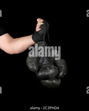 Le bras de l'homme enveloppé dans un bandage élastique noir sports détient old vintage paire de gants de boxe en cuir, fond noir, copy space Banque D'Images