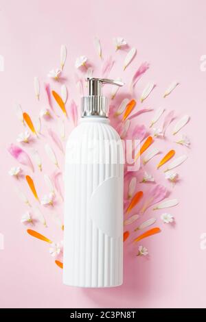 Pulvérisateur cosmétique avec pétales de fleur sur fond rose Banque D'Images