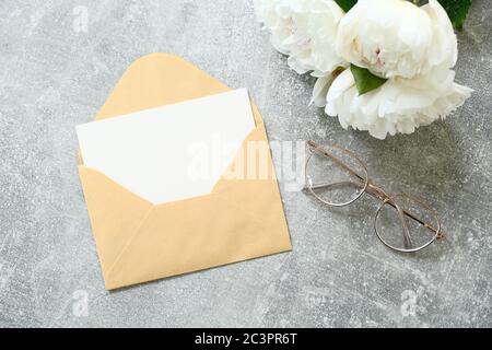 Concept de lettre d'amour. Enveloppe avec maquette vierge de carte blanche, bouquet de fleurs de pivoines et verres sur fond de pierre. Compos de style décontracté romantique Banque D'Images