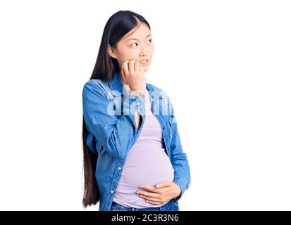 Jeune belle femme chinoise enceinte s'attendant à bébé regardant stressé et nerveux avec les mains sur la bouche piquant des ongles. Problème d'anxiété. Banque D'Images
