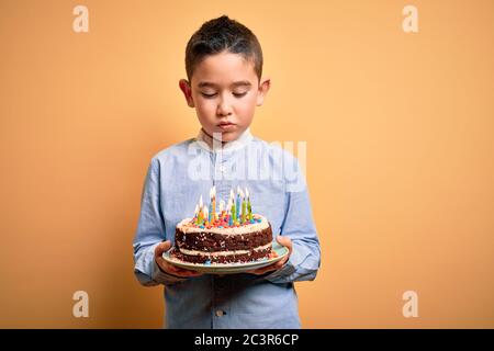 Adorable tout-petit portant un gâteau d'anniversaire avec des bougies sur fond jaune isolé Banque D'Images