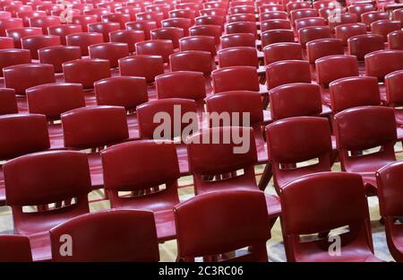 Des masses de rouge moulé masse produite des chaises de style d'école en plastique soigneusement aligné en rangées vides prêt pour l'assemblage ou une convention Banque D'Images