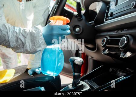 vue de culture d'un spécialiste en costume de noisette nettoyant l'intérieur de la voiture avec un spray antiseptique pendant une pandémie de coronavirus Banque D'Images