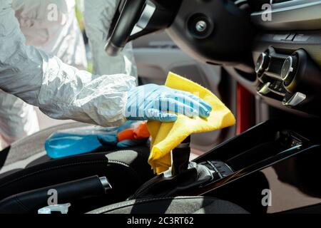 vue rognée du spécialiste en costume de noisette nettoyage intérieur de voiture avec un spray et un chiffon pendant une pandémie de coronavirus Banque D'Images