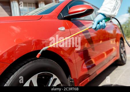 vue en coupe d'un spécialiste de la voiture de nettoyage de combinaison de matières dangereuses avec spray désinfectant pendant la pandémie de covid-19 Banque D'Images