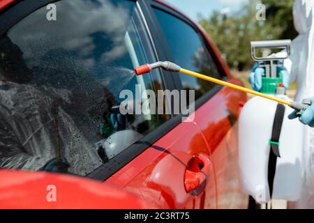 vue en coupe d'un travailleur professionnel dans une voiture de nettoyage avec un désinfectant dans un sac de pulvérisation pendant une pandémie de covid-19 Banque D'Images