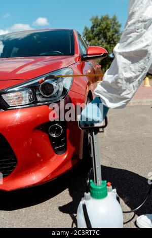 vue en coupe du travailleur dans une voiture de nettoyage avec un désinfectant dans un sac de pulvérisation pendant une pandémie de coronavirus Banque D'Images