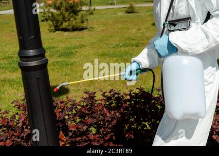 vue rognée du spécialiste de la combinaison de matières dangereuses et du respirateur désinfectant le lampadaire dans le parc pendant une pandémie de coronavirus Banque D'Images