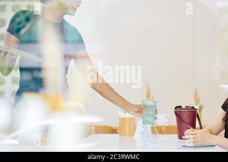 Serveur femme souriante mettant un verre d'eau devant la cliente avant de prendre la commande Banque D'Images
