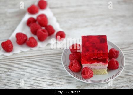 Gâteau à la framboise sur une assiette blanche avec de la gélatine rouge sur le dessus décoré de framboises fraîches, en arrière-plan fruits frais en douceur Banque D'Images