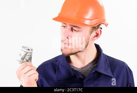 Un homme dans un casque a reçu un pot-de-vin, de l'argent pour un travail illégal. Le constructeur gagne de l'argent, le réparateur conserve de l'argent, des billets en dollars en main. Travail illégal, concept. Beau visage strict, fond blanc. Banque D'Images