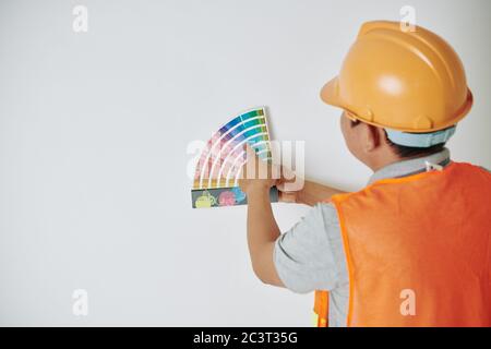 Ouvrier de construction en casque et veste orange choisir la couleur de la palette avec des nuances Banque D'Images