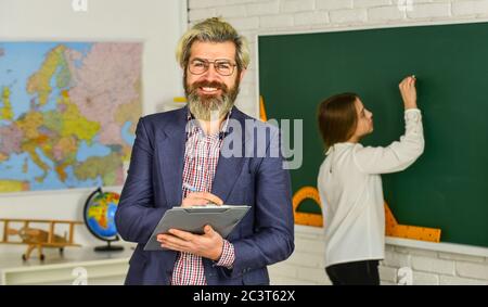 Enseignant vérifiant la bonne réponse. Enseigner avec passion. Matériel pédagogique. Qui est absent aujourd'hui. Petite fille au tableau noir. Retour à l'école. Étudiant et enseignant en classe. Suivez la progression des étudiants. Banque D'Images