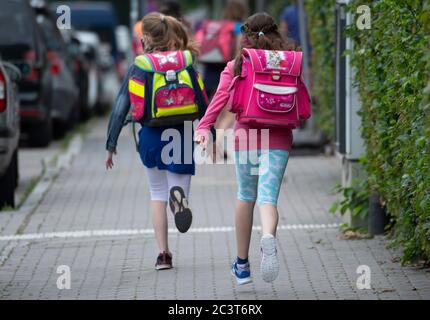 22 juin 2020, Hessen, Francfort-sur-le-main : deux élèves d'une école primaire courent les derniers mètres jusqu'à la cour d'école avec une sacoche sur le dos. À partir de lundi, les élèves de l'école primaire de Hesse seront de nouveau autorisés à assister à des cours ensemble après des mois de restrictions. Photo : Boris Roessler/dpa Banque D'Images