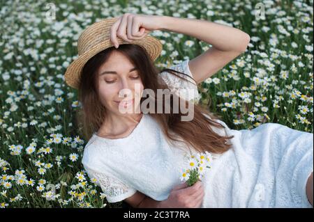 Belle femme appréciant champ de camomille, belle femme couché dans le pré de fleurs, jolie fille se relaxant en plein air, s'amuser, bonne jeune femme Banque D'Images