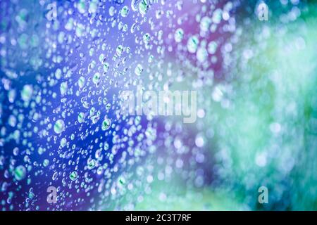 Pluie tombe sur la fenêtre avec arbre violet-vert abstrait en arrière-plan. Banque D'Images