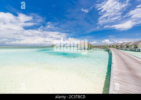 Paradis tropical : vue sur les bungalows sur l'eau dans un complexe des Maldives, Océan Indien. Longue jetée menant à des villas aquatiques sous un ciel tropical bleu Banque D'Images