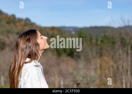 Souriante, jolie jeune femme avec un sweat-shirt qui respire l'air pur dans la nature et bronzer les montagnes derrière Banque D'Images