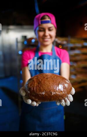 Une petite fille prend du pain chaud dans une boulangerie contre le fond de rayonnages avec du pain. Production industrielle de pain. L'étape de la cuisson dans une boulangerie Banque D'Images