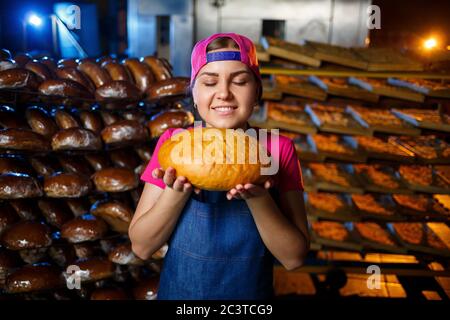 La phase de cuisson dans une boulangerie. Portrait d'une petite fille avec du pain dans ses mains contre le fond des étagères dans une boulangerie. Mains d'un boulanger avec humour Banque D'Images