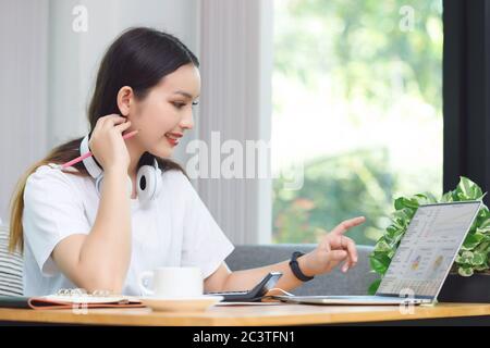 Femme asiatique étudiante assise à la table dans le salon, en utilisant un ordinateur portable pour étudier en ligne Banque D'Images