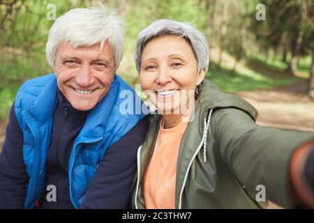 Portrait de POV de couple senior actif regardant l'appareil photo et souriant tout en prenant photo selfie pendant la randonnée dans la forêt d'automne, espace de copie Banque D'Images