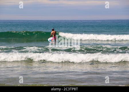 Semelle debout paddle boarder s'agenouiller tout en pagayant contre les vagues pour aller à la mer Santona Cantabria Espagne Banque D'Images