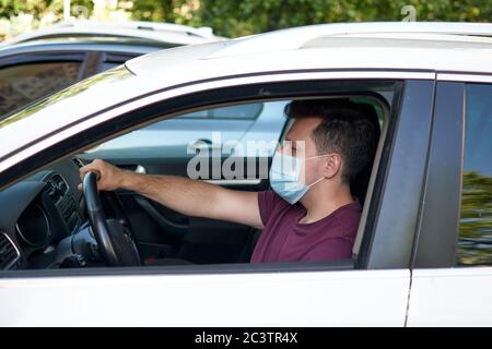 Un homme conduisant une voiture dans un masque médical pendant l'épidémie de coronavirus, un chauffeur de taxi dans un masque, protection contre le virus. Quarantaine, Covid-19. Banque D'Images