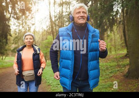 Portrait en vue avant d'un couple senior actif en forêt, concentrez-vous sur le sourire, le port d'un casque et la musique Banque D'Images