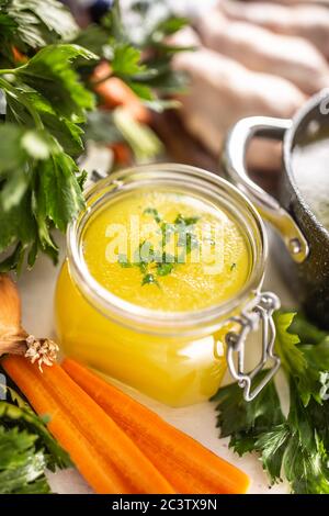 Bouillon de poulet dans un pot en verre, cuisses de poulet crues, carottes, oignons, céleri, herbes, ail et légumes frais Banque D'Images