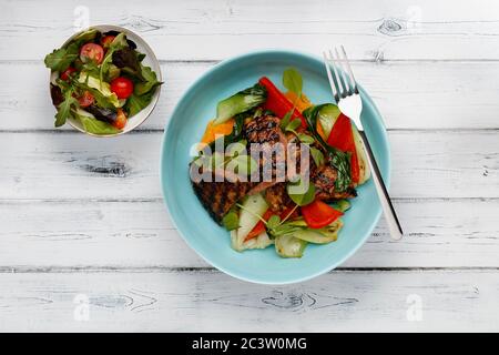 Un délicieux bol de filet de steak de rumsteck, purée de potatoe douce, poivrons rouges et légumes, dans un bol bleu clair avec une salade d'accompagnement, sur un blanc vieilli Banque D'Images