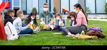 Groupe d'enfants gaies avec masques de visage apprenant à l'extérieur à l'école après le verrouillage. Banque D'Images