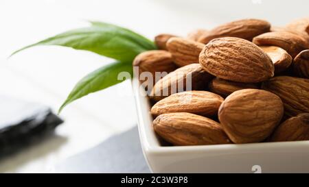 amandes dans une assiette blanche sur un plateau noir sur une table en bois, gros plan Banque D'Images