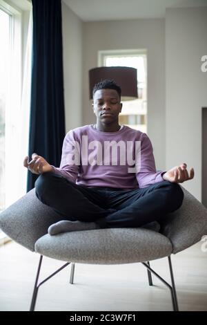 Adolescent pacifique méditant Sitting in Chair At Home Banque D'Images