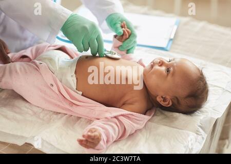 Gros plan d'un médecin méconnaissable examinant un bébé mixte mignon allongé sur une table à langer en clinique, espace de copie Banque D'Images