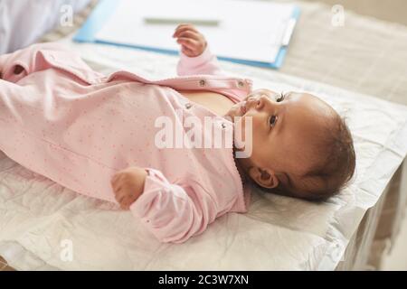 Portrait ton chaud de petite fille mignonne couché sur table à langer au bureau de médecins en onesie rose, espace de copie Banque D'Images