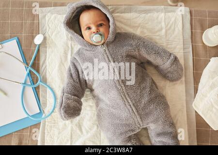 Vue de dessus en bas sur un joli bébé afro-américain portant une combinaison en peluche couché sur une table à langer pendant le contrôle au bureau du médecin, espace de copie Banque D'Images